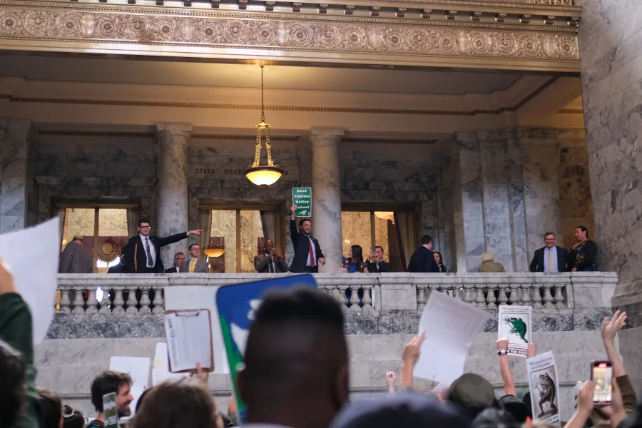 WFSE protesters in the Washington State Capitol Building hold up signs towards a representative on the balcony with a "Save Yakima Valley School" sign