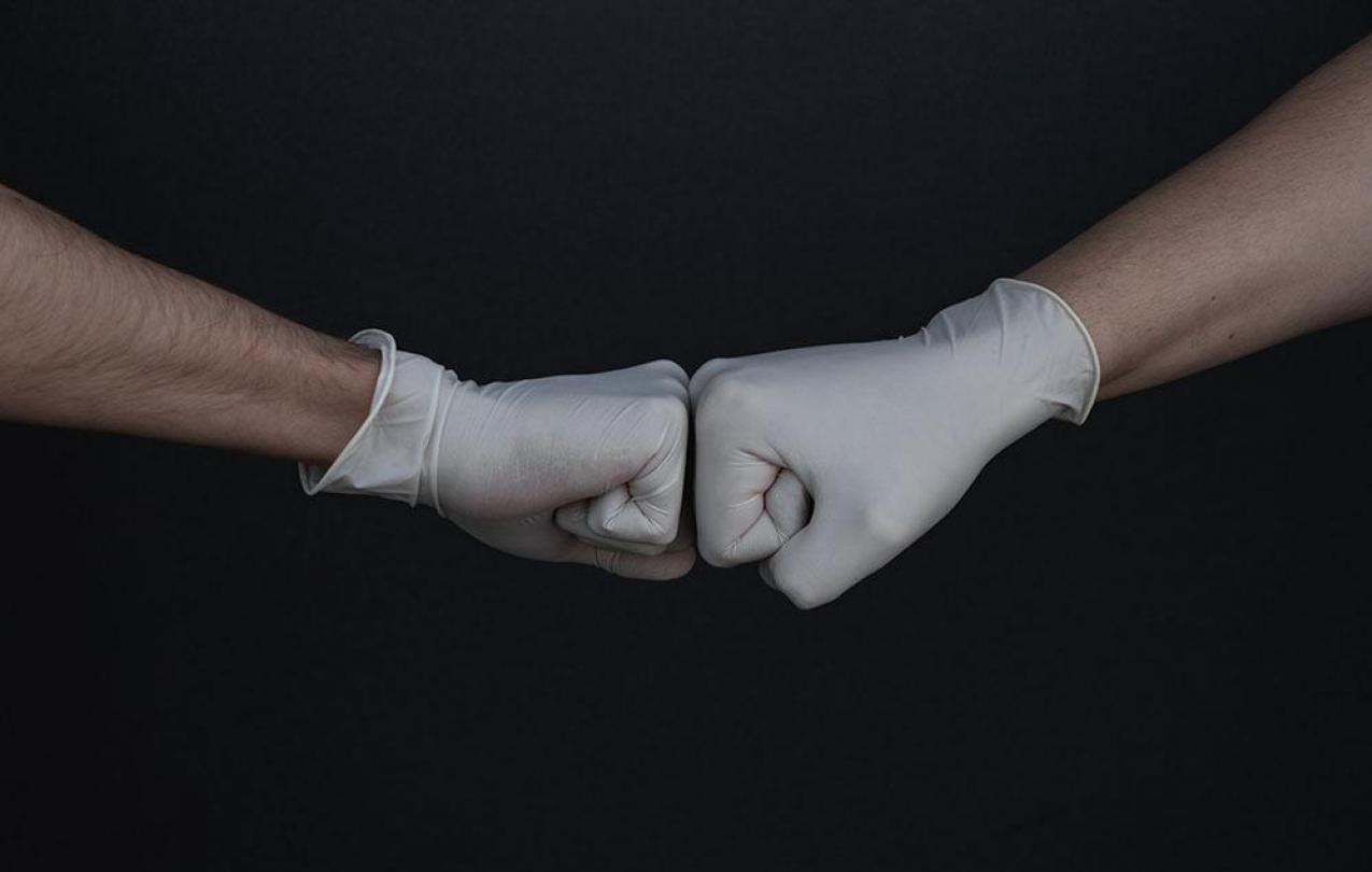 Two hands with light skin wearing medical gloves do a fist bump