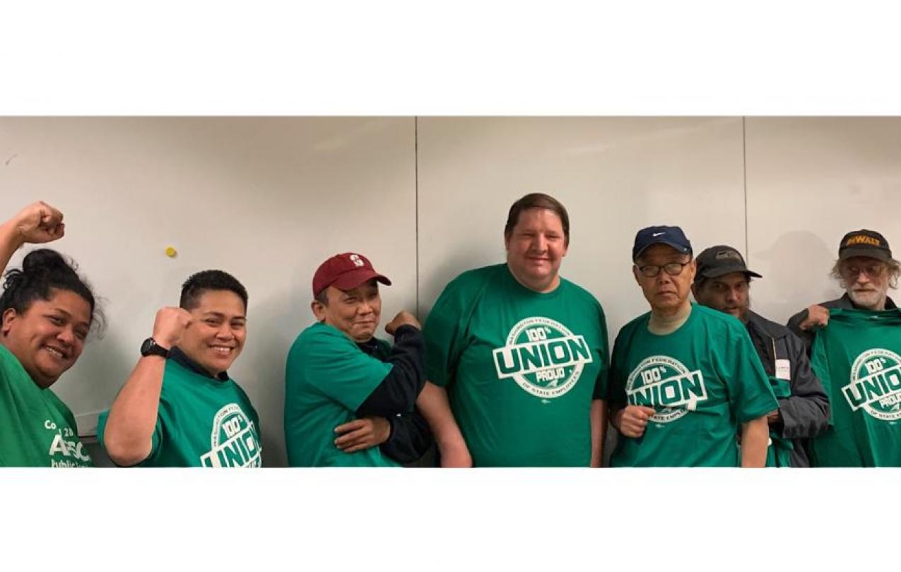 A group of Bellevue College custodians wearing WFSE shirts pose against a wall and smile.