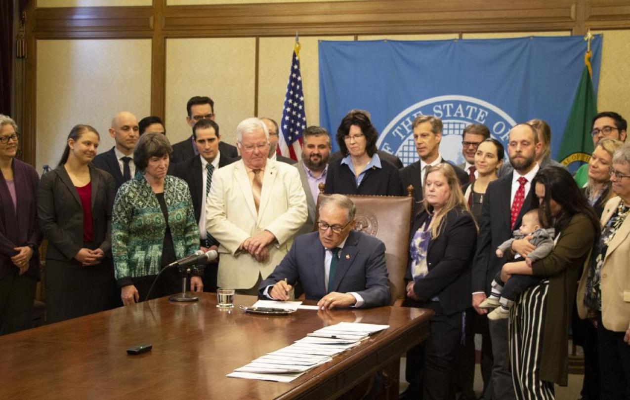 Governor Inslee signs Senate Bill 5297 as a group of Assistant Attorneys General watches