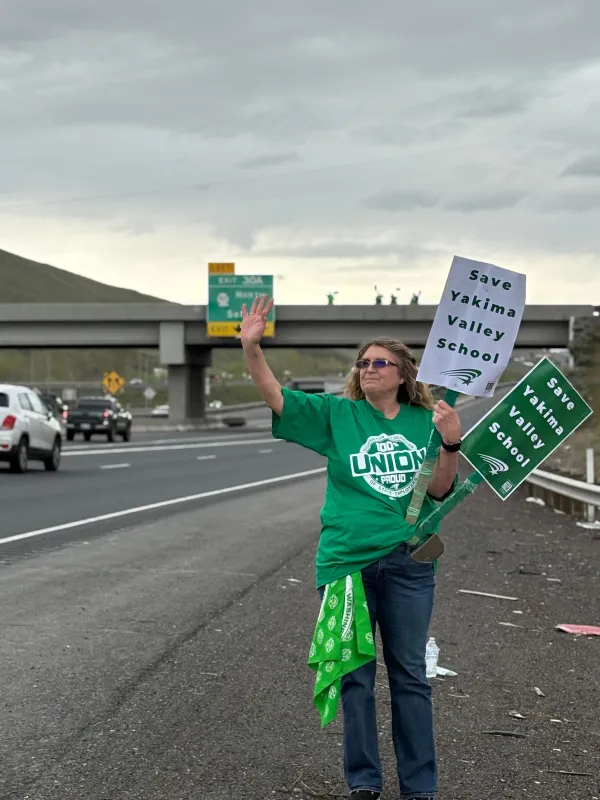 A WFSE member stands on a busy roadside with signs fighting to save Yakima Valley School