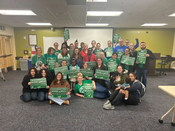 A group of WFSE members at Everett Community College pose with signs at a Board of Trustees meeting for the EvCC ELC.